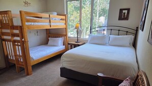 Une chambre avec un lit superposé, un lit simple, une chaise en bois et une table de chevet avec une lampe.