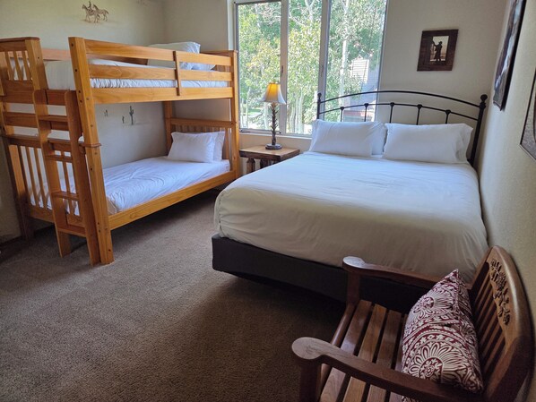 A room with a bunk bed, a single bed, a wooden chair, and a nightstand with a lamp.