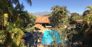 A house with a swimming pool surrounded by tropical vegetation and mountains in the background. - Suites em Meio a Mata Atlantica (Petrópolis)