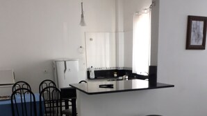 A modern kitchen with a central island, two bar stools, a dining area with chairs, and a refrigerator.