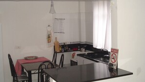 A small kitchen with a black countertop, a dining table with chairs, and a red and white checkered tablecloth.
