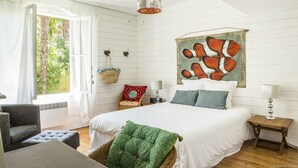 Un dormitorio con cama, almohadas, lámpara colgante, un cuadro en la pared y ventana con cortinas.