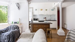 Una habitación acogedora con cama, una silla y vistas a una cocina con armarios blancos y piso de madera.