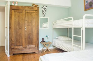 Un dormitorio con un armario de madera, literas, una mesita con lámpara y una estantería en la pared.