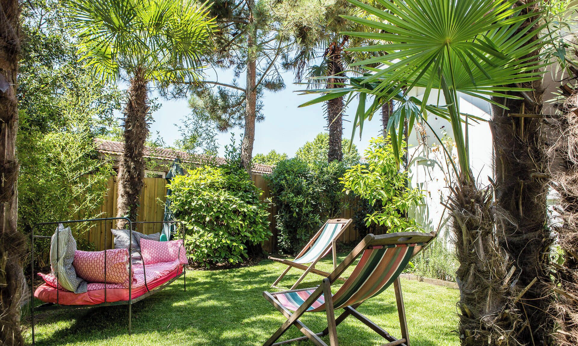 Un jardin agrémenté d’un hamac, de deux chaises longues et d’une variété d’arbres et d’arbustes.