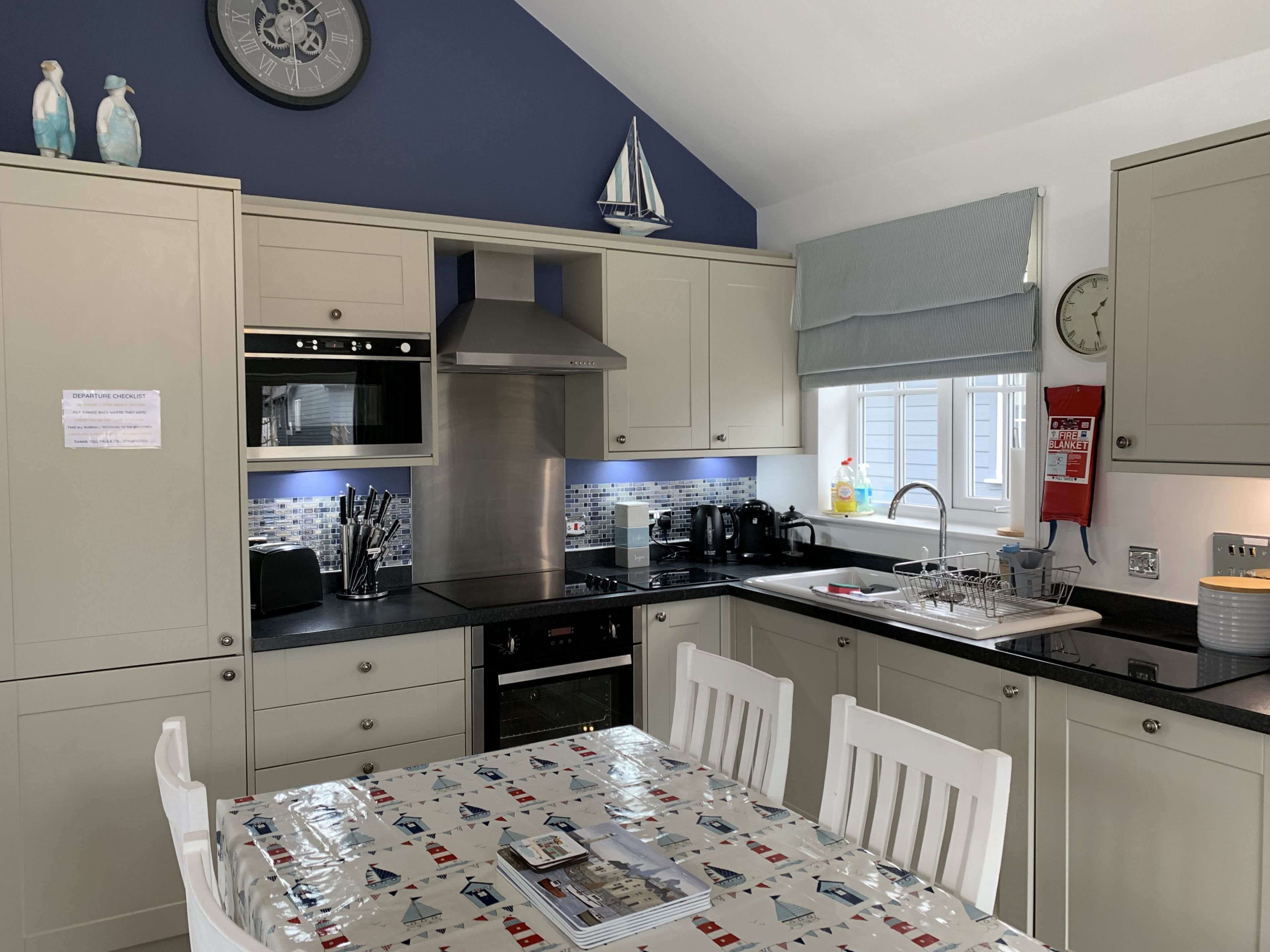 Une cuisine moderne avec des meubles blancs, des appareils en acier inoxydable et une table à manger recouverte d’une nappe protectrice.