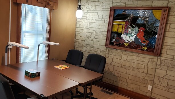 Una sala de conferencias con una mesa de madera, sillas negras, una obra de arte enmarcada y un ventanal con persianas.
