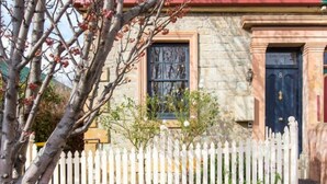 Un bâtiment en pierre avec une porte bleu foncé et une clôture en bois peinte en blanc.
