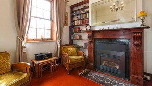 Une pièce chaleureuse avec une cheminée, une bibliothèque, un fauteuil confortable et une petite table.
