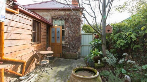 Une maison en bois avec une terrasse carrelée, une petite table et des chaises, et un nichoir.