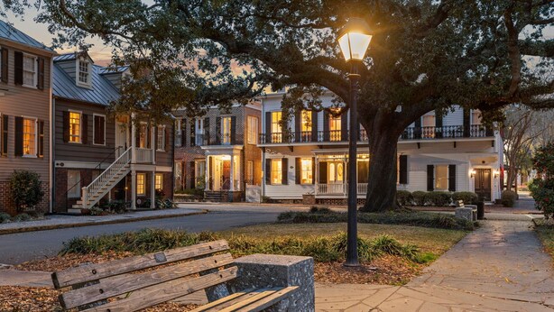 A row of townhouses with front porches, a stone bench, and a street lamp.