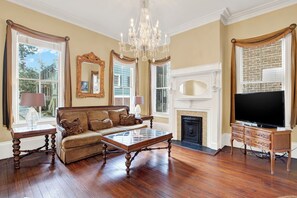 A spacious living room with a large sofa, a glass coffee table, a fireplace, and a television on a wooden stand. - Heated Pool Access | 5*Clean | Flex Cancelation (Savannah)