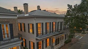 A two-story building with a balcony, brick foundation, and multiple windows with shutters.