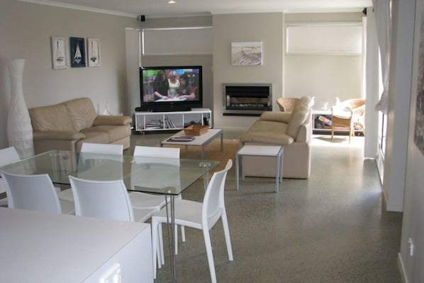 Ein modernes Wohnzimmer mit einem Glastisch, zwei beigefarbenen Sofas, einem Flachbildfernseher und einem Kamin.