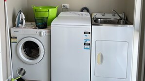 Pesuhuone, jossa on pesukone, kuivausrumpu ja seinälle kiinnitetty kello.