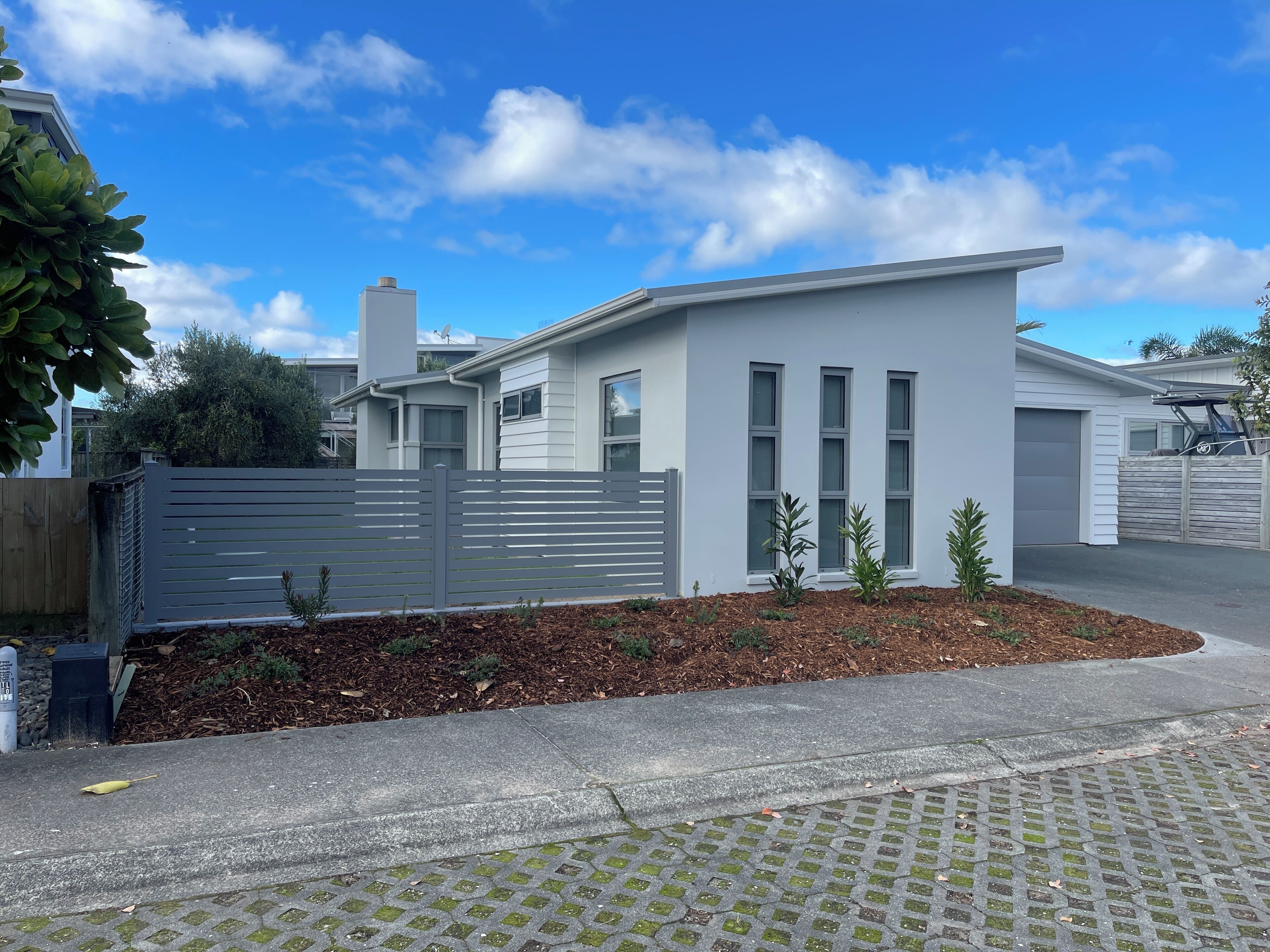 A modern two-story house with a grey exterior, a fenced yard, and a clear blue sky.
