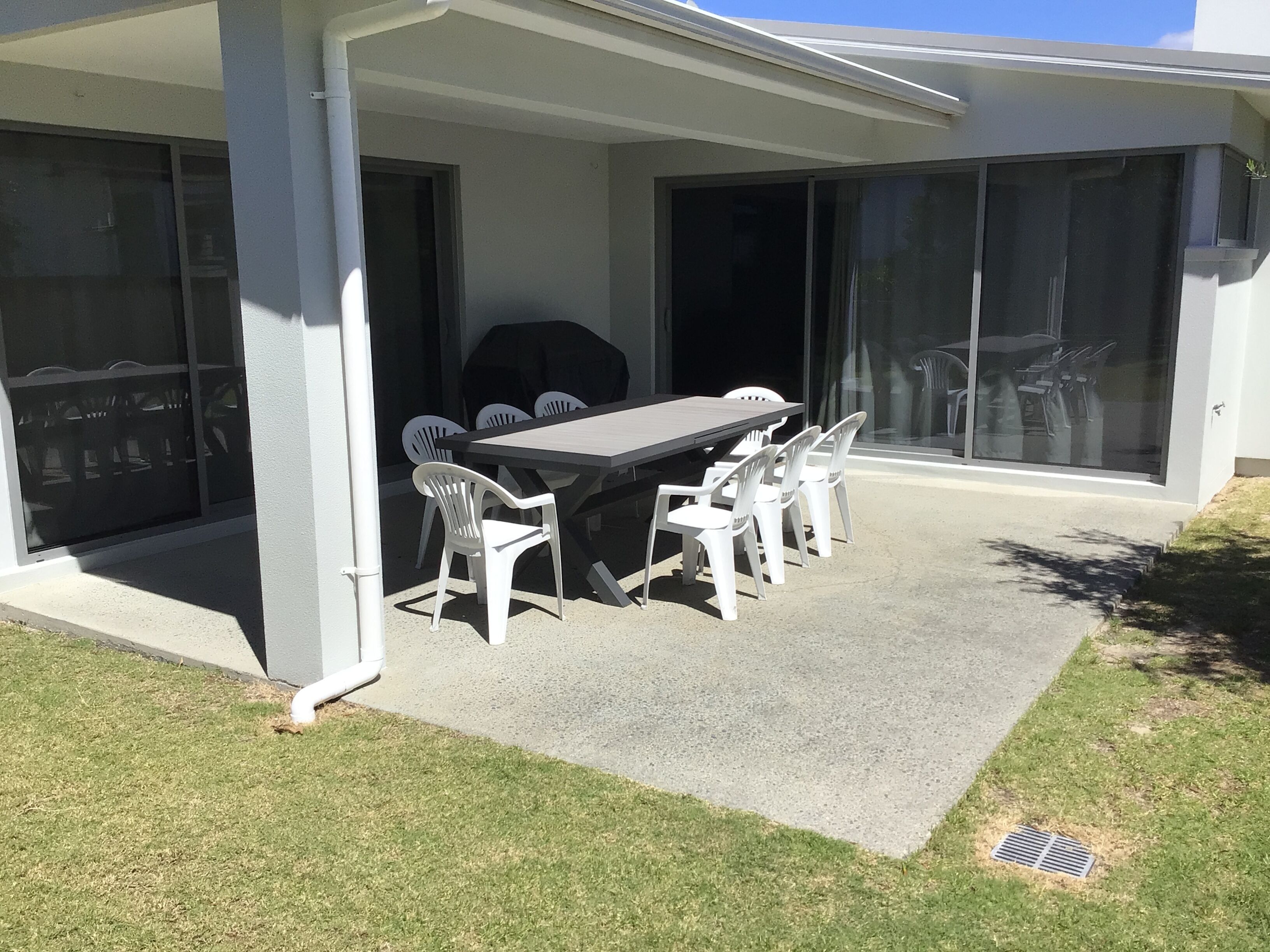 Un patio exterior con mesa y sillas, una parrilla y una zona cubierta con puertas corredizas de vidrio.