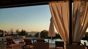 Un espace aménagé au bord de la piscine, avec des chaises longues et un parasol, offrant une vue sur une étendue d’eau et des collines lointaines.