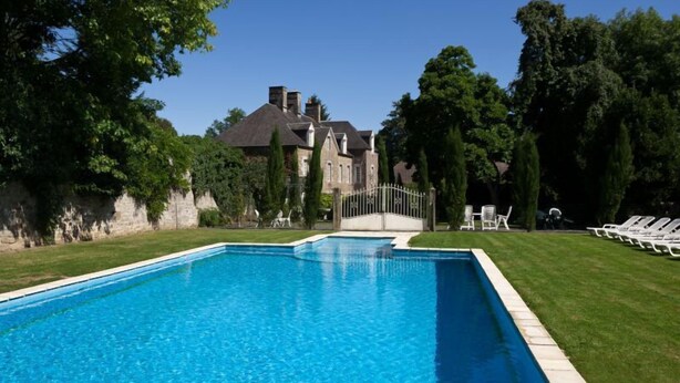 A rectangular swimming pool with a stone border, surrounded by a well-maintained lawn and trees.