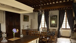 A dining area with a wooden table and chairs, a chandelier, and a window with curtains.