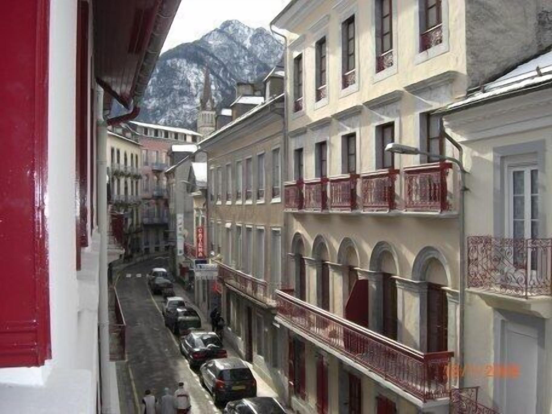 A narrow street with parked cars and buildings with balconies.