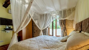 Une chambre à coucher avec un lit, des rideaux blancs, un mur en pierre et un téléviseur fixé au mur.
