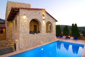 Un edificio de piedra con piscina, mobiliario exterior y vistas a las colinas.