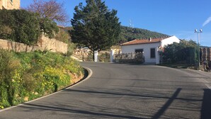 A curved road with a stone wall on one side and a white building with a tiled roof on the other.