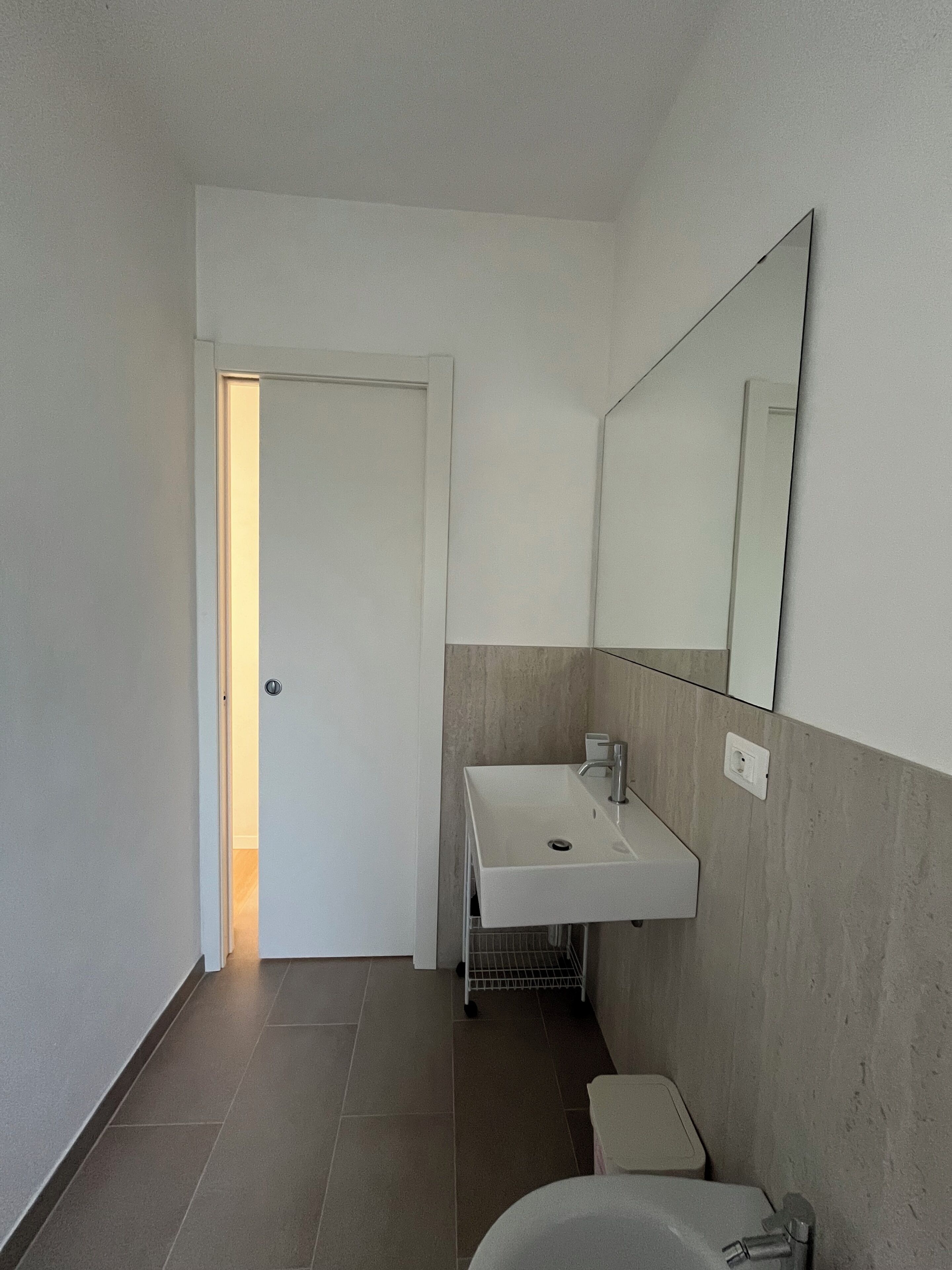 Un baño con un lavamanos blanco, un espejo, un inodoro y una puerta que da a otra habitación.