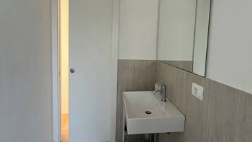 Un baño con un lavamanos blanco, un espejo, un inodoro y una puerta que da a otra habitación.
