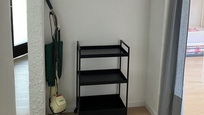 Una habitación en esquina con un estante metálico negro, un aspirador y una pared blanca con textura.