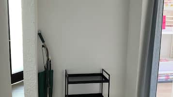 Una habitación en esquina con un estante metálico negro, un aspirador y una pared blanca con textura.