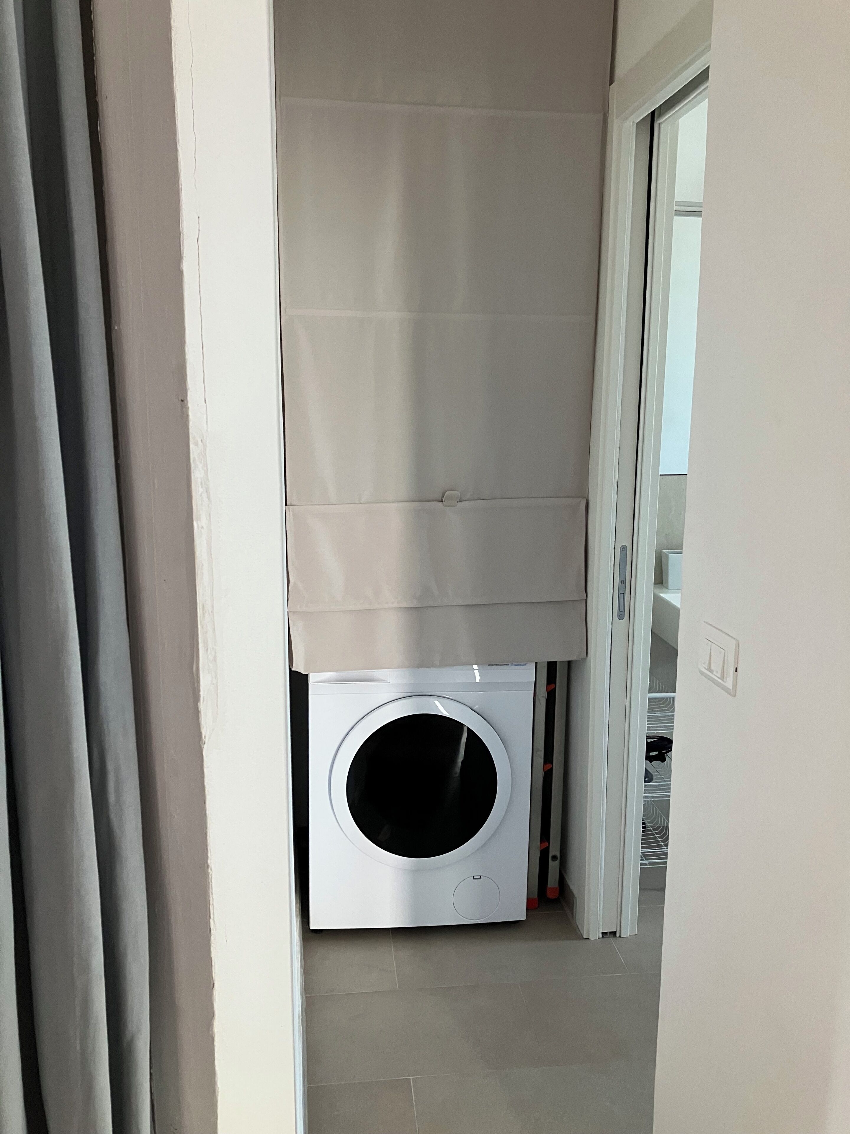Una lavanderia con lavatrice, una tenda e una porta che dà su un'altra stanza.