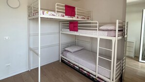 Habitación con literas, suelo de madera, paredes blancas y un espejo a la derecha.