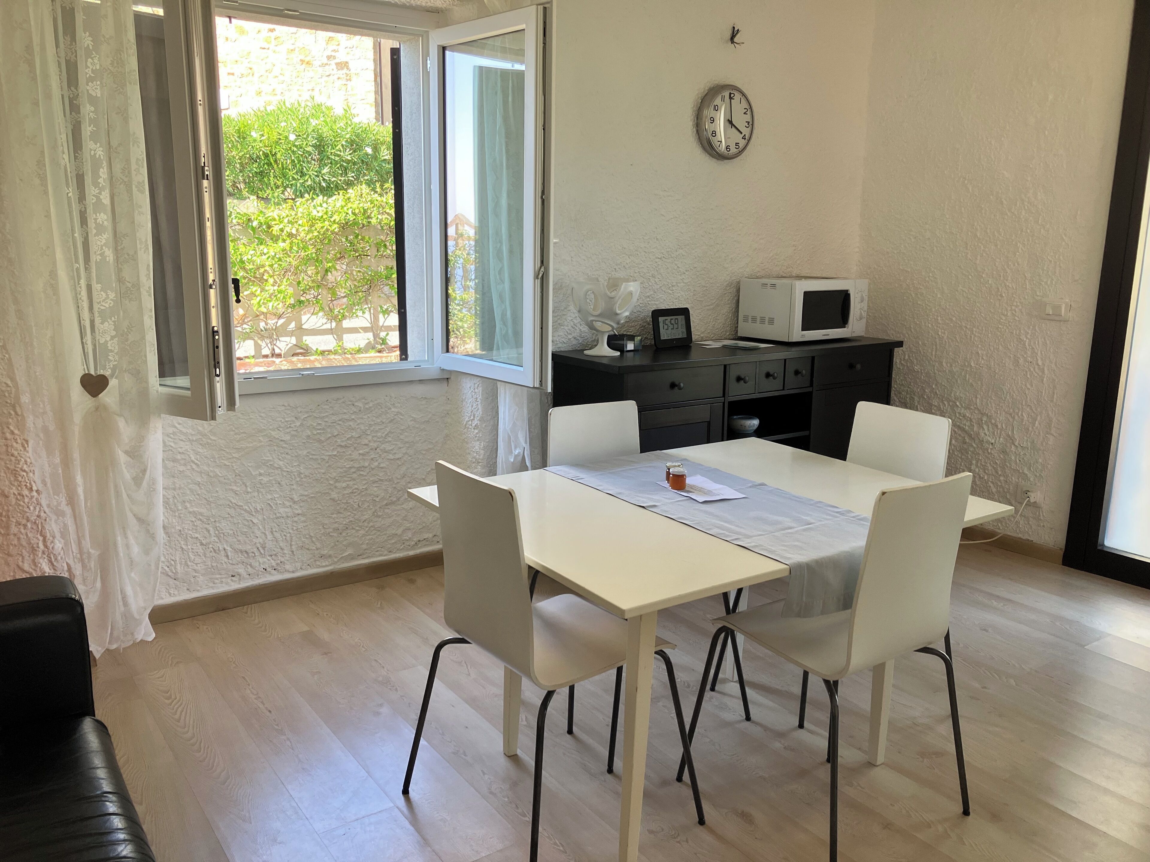 Comedor con una mesa, sillas, un reloj y vistas al follaje exterior.