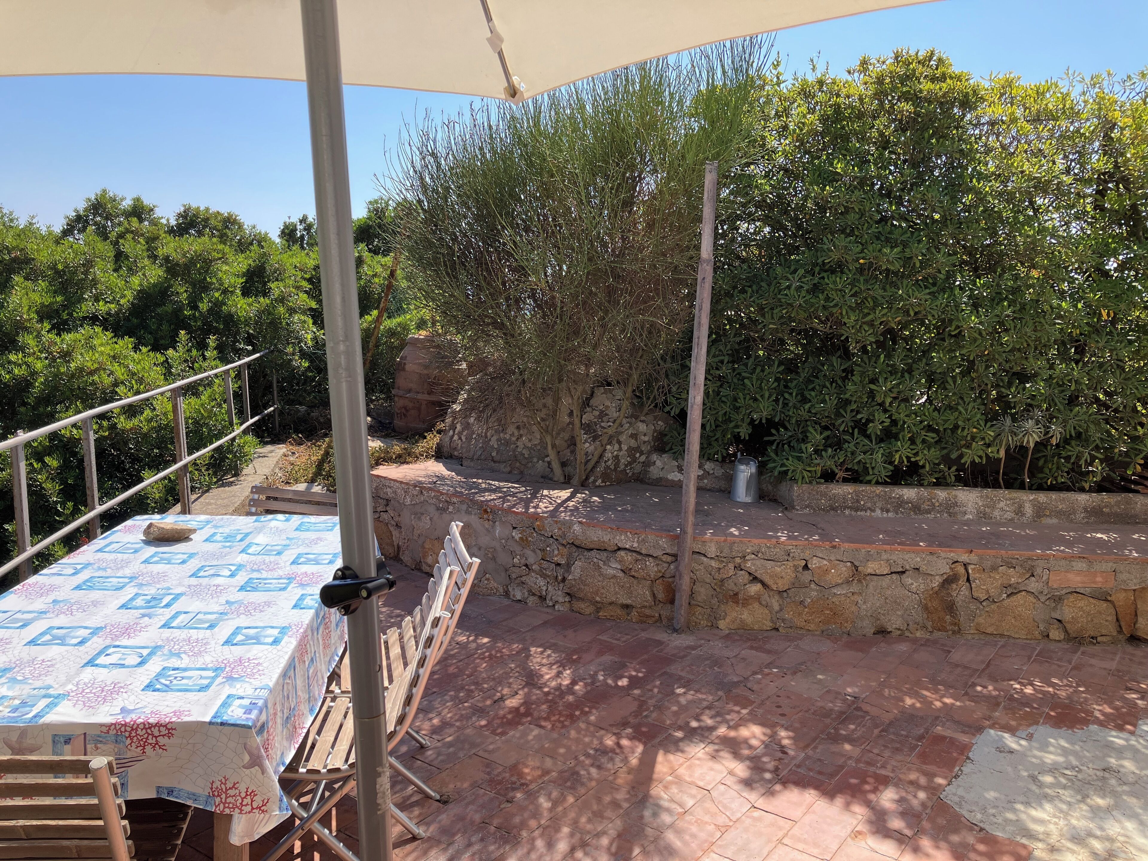 Eine Terrasse im Freien mit Esstisch, umgeben von Steinmauern und Grünpflanzen.