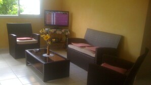 A living room with a sofa, two armchairs, a coffee table with a vase of flowers, and a television on a stand. - Bottom of villa for rent in diamond (F3) (Diamant)