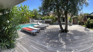 A wooden deck with lounge chairs, a swimming pool, and a garden area with various plants and a barbecue grill.