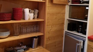 Ett kompakt kök med träinredning, ett inbyggt kylskåp och hyllor där olika köksredskap förvaras.