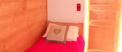 A small, single-bed room with a wooden headboard, a red bedspread, and a pillow with a heart design.