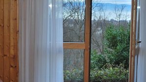 Un dormitorio con una cama grande, una ventana con vistas a árboles y una masa de agua, y paneles de madera en las paredes.