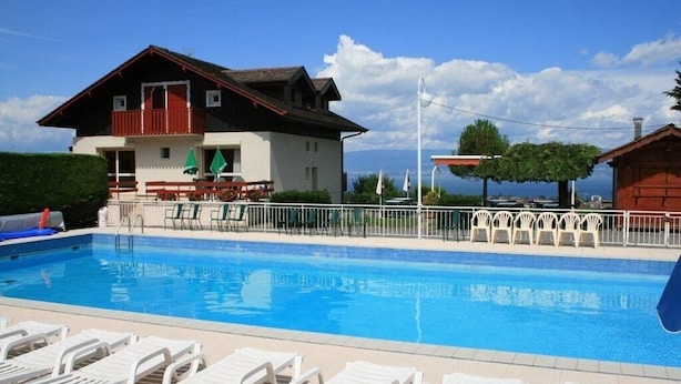 Una piscina con sillas de descanso, un edificio con balcón y vistas al mar.