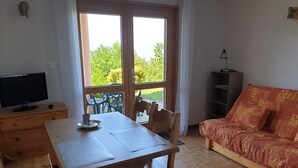 Una habitación con un escritorio de madera, televisión, sofá y un ventanal con vistas a zonas verdes.