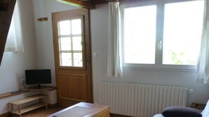 Et værelse med trælofter, en seng med pude, et træskrivebord med en computer, et vindue med gardiner og en radiator.