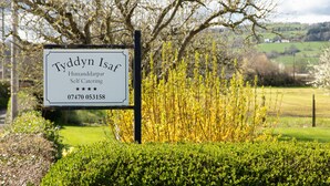 A sign for 'Tyddyn Isaf' indicating self-catering accommodation with a contact number. - Views Of The Clwydian Range, Nr Ruthin. Snowdonia 1hr. Local pub 1 mile (Rhewl)