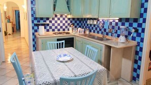 Een keuken met blauwgroene kastjes, een geruit spatwand en een tafel met een kanttafelkleed.