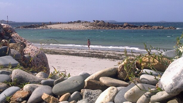 Une plage au rivage rocheux, où une personne se promène le long du bord de l’eau.
