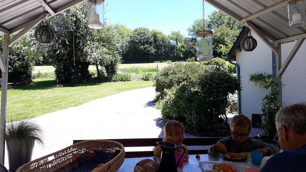 Un área de comedor al aire libre con techo, una mesa dispuesta para cuatro personas, rodeada de vegetación y vistas despejadas al exterior.