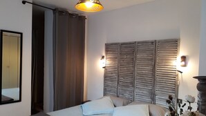Un dormitorio con cama, cortinas, un espejo, luces empotradas en la pared y un jarrón decorativo con flores.
