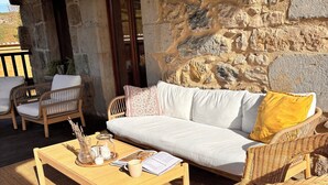 Un espacio exterior acogedor con mobiliario de mimbre, una mesa de madera y un muro de piedra de fondo.